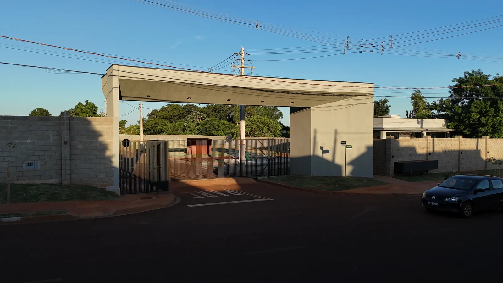 Portal de acesso do Flor de Maio 4 com portões de grade e muro no perímetro