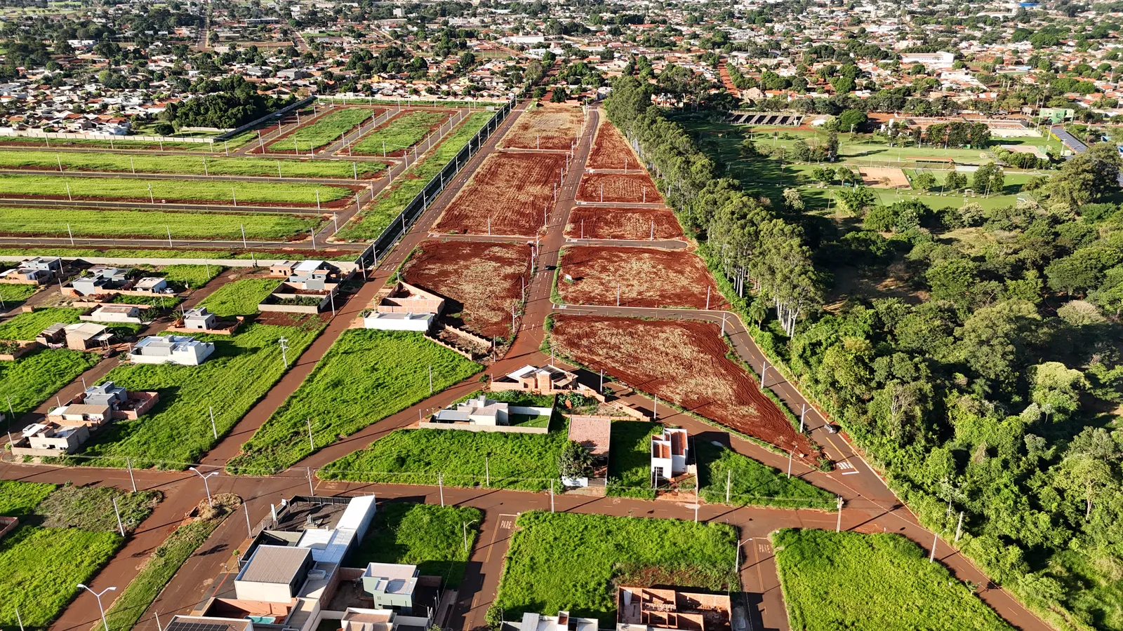 Lotes e ruas asfaltadas do Ouro Branco Loteamento Aberto, com casas construídas na vizinhança e a cidade de Dourados ao fundo